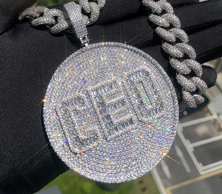 Round silver-tone CEO pendant hanging from a Cuban chain