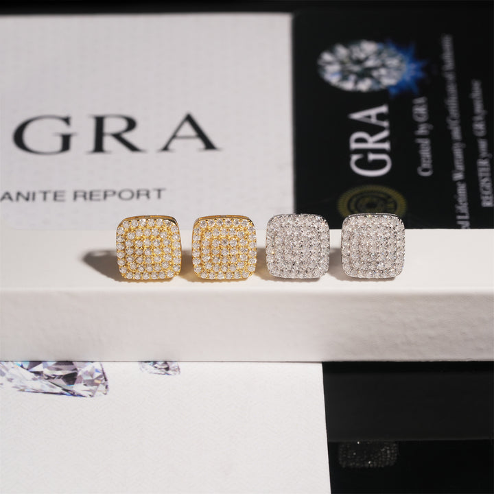Gold-tone and silver-tone rounded-square stud earrings on a box beside GRA cards