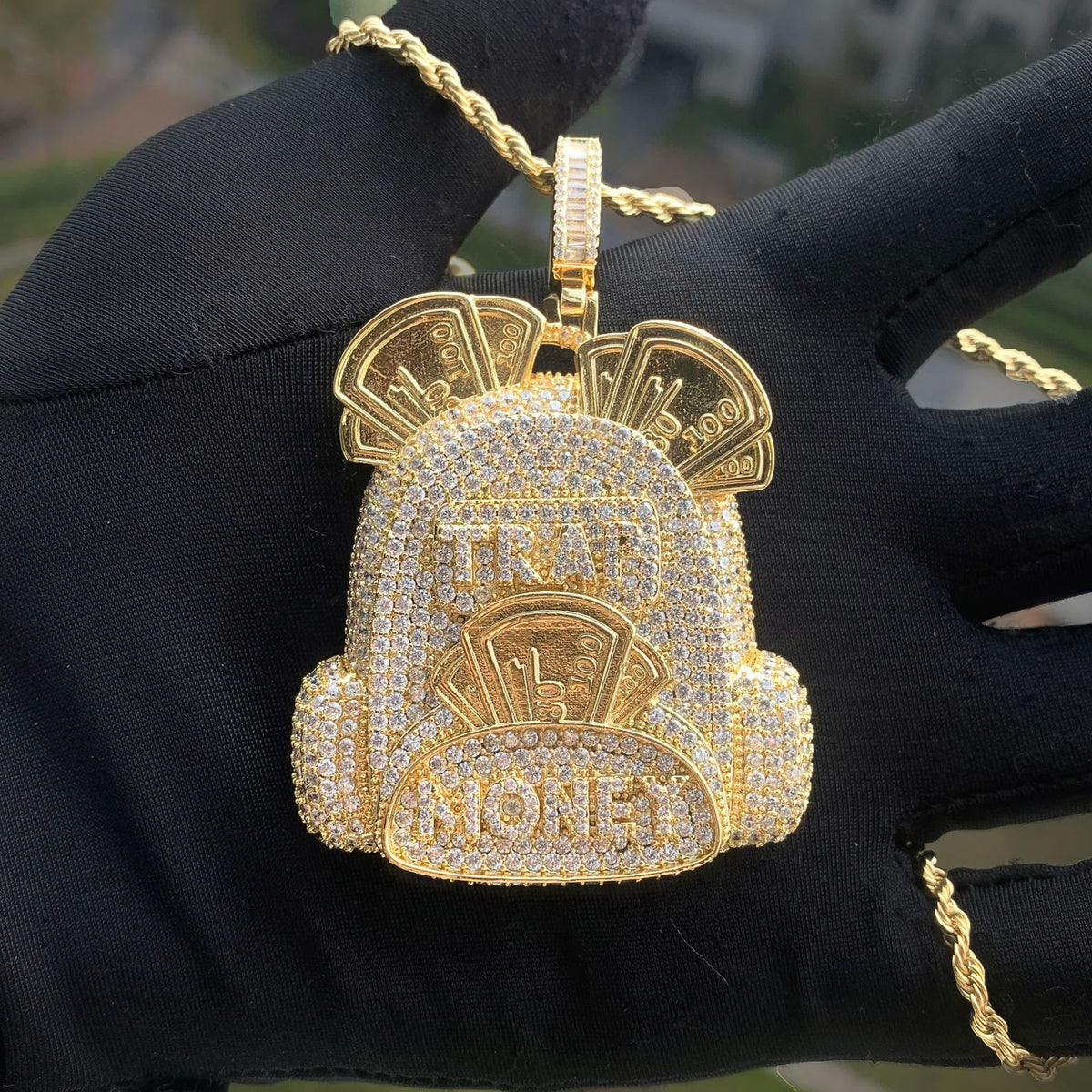 Gold-tone backpack pendant displayed on a black glove outdoors