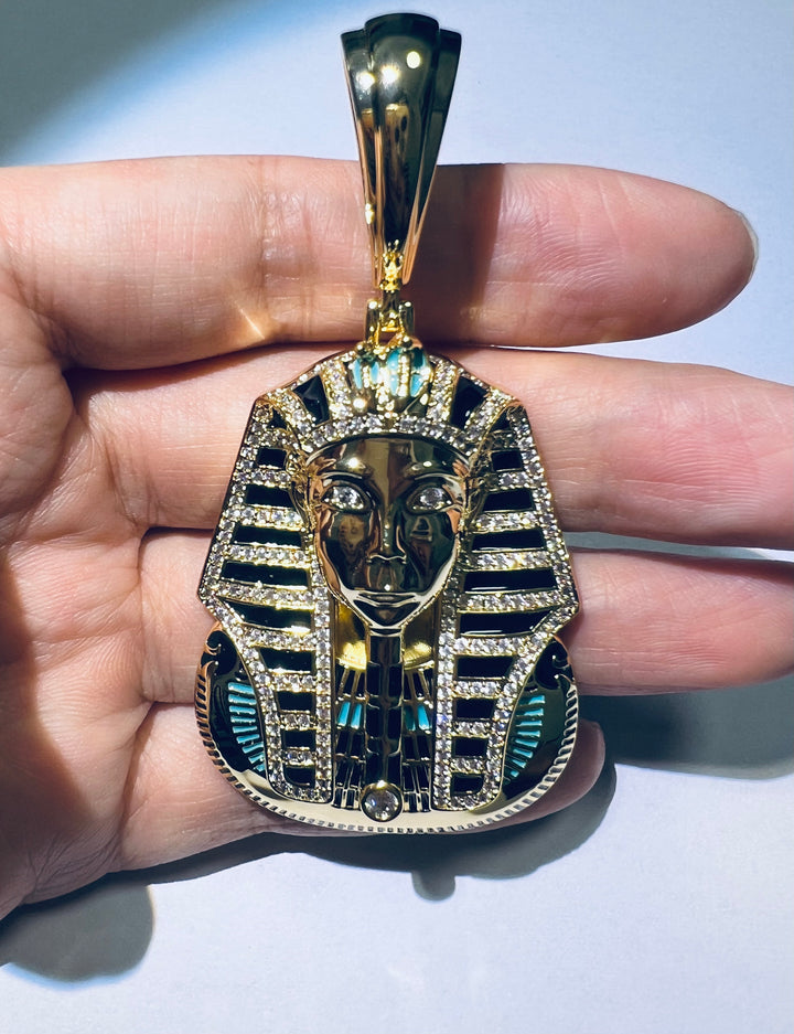 Gold-tone pharaoh head pendant with dark accent stones held in a hand