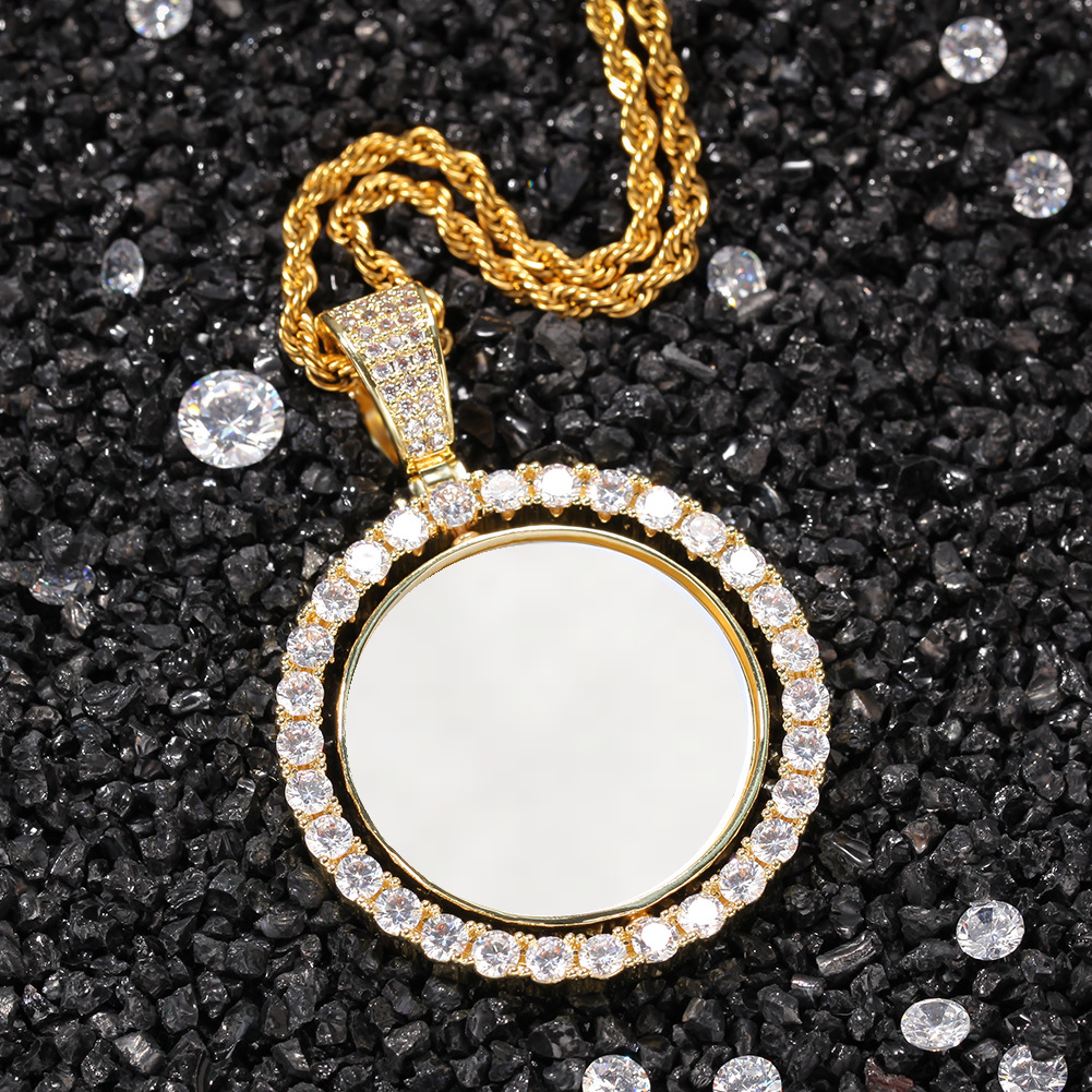 Gold-tone photo pendant with a white photo area on dark gravel beside loose faceted stones