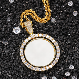 Gold-tone photo pendant with a white photo area on dark gravel beside loose faceted stones