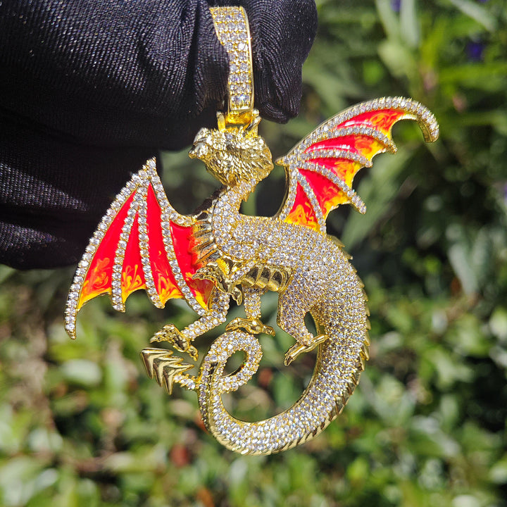 Gold-tone dragon pendant held by a black glove, showing red-and-yellow wings