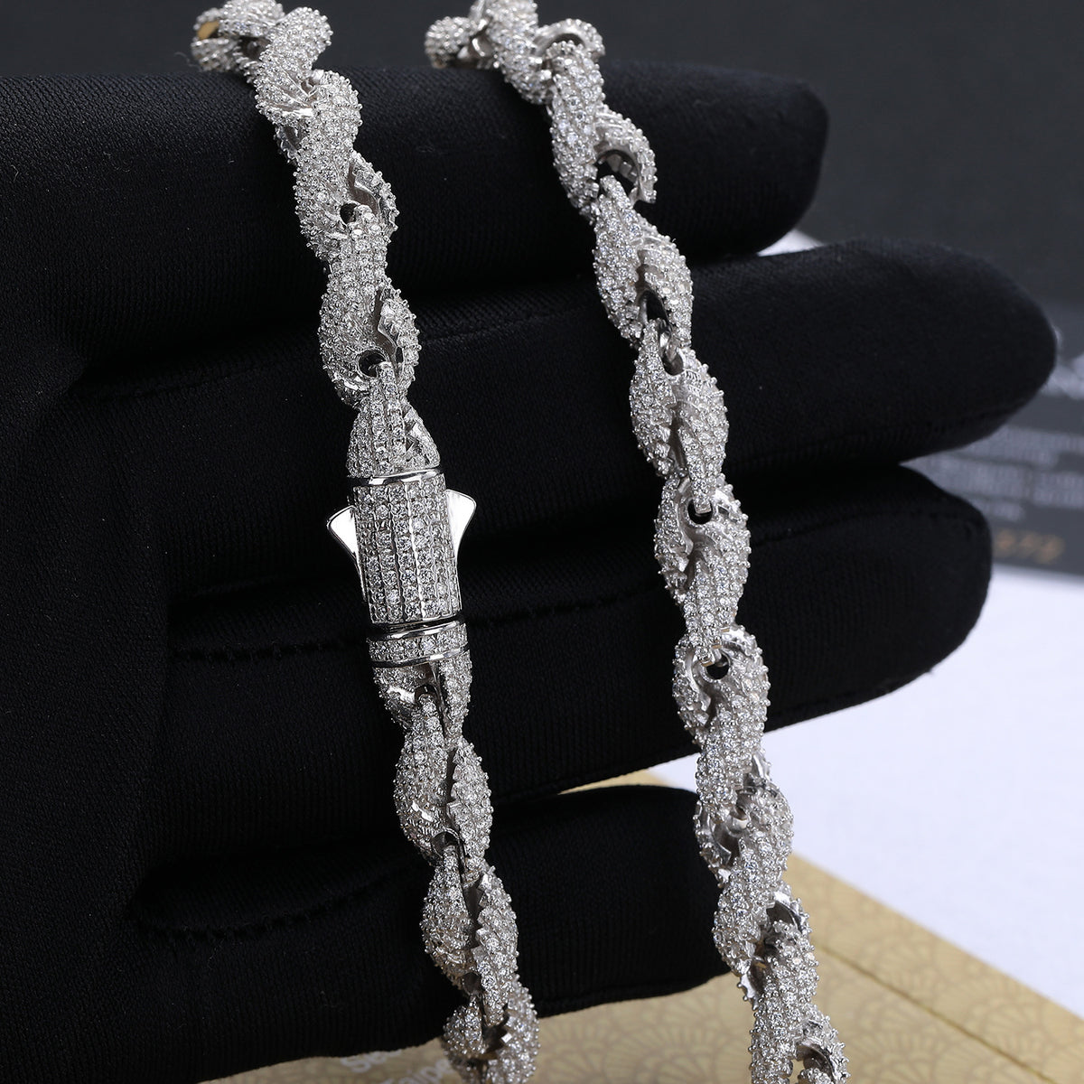 Close view of silver-tone rope links and a closed box clasp held against a black glove