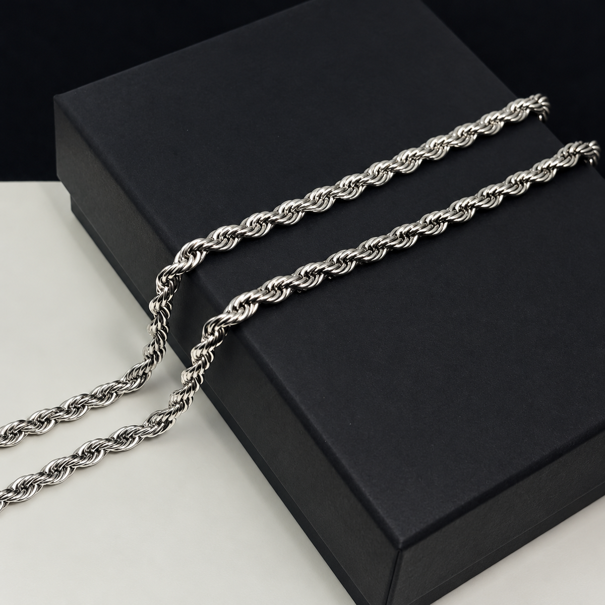 Close-up of a silver-tone rope chain draped on an unbranded black box