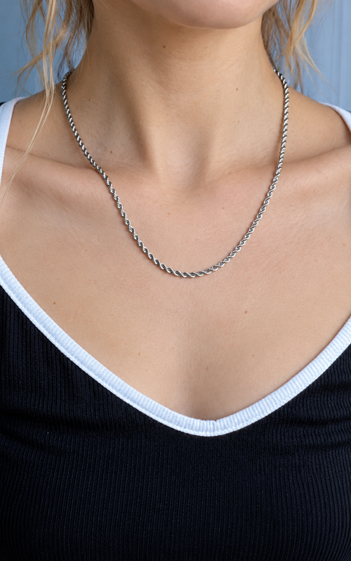 Model wearing a slender silver-tone rope chain above a dark top with white trim