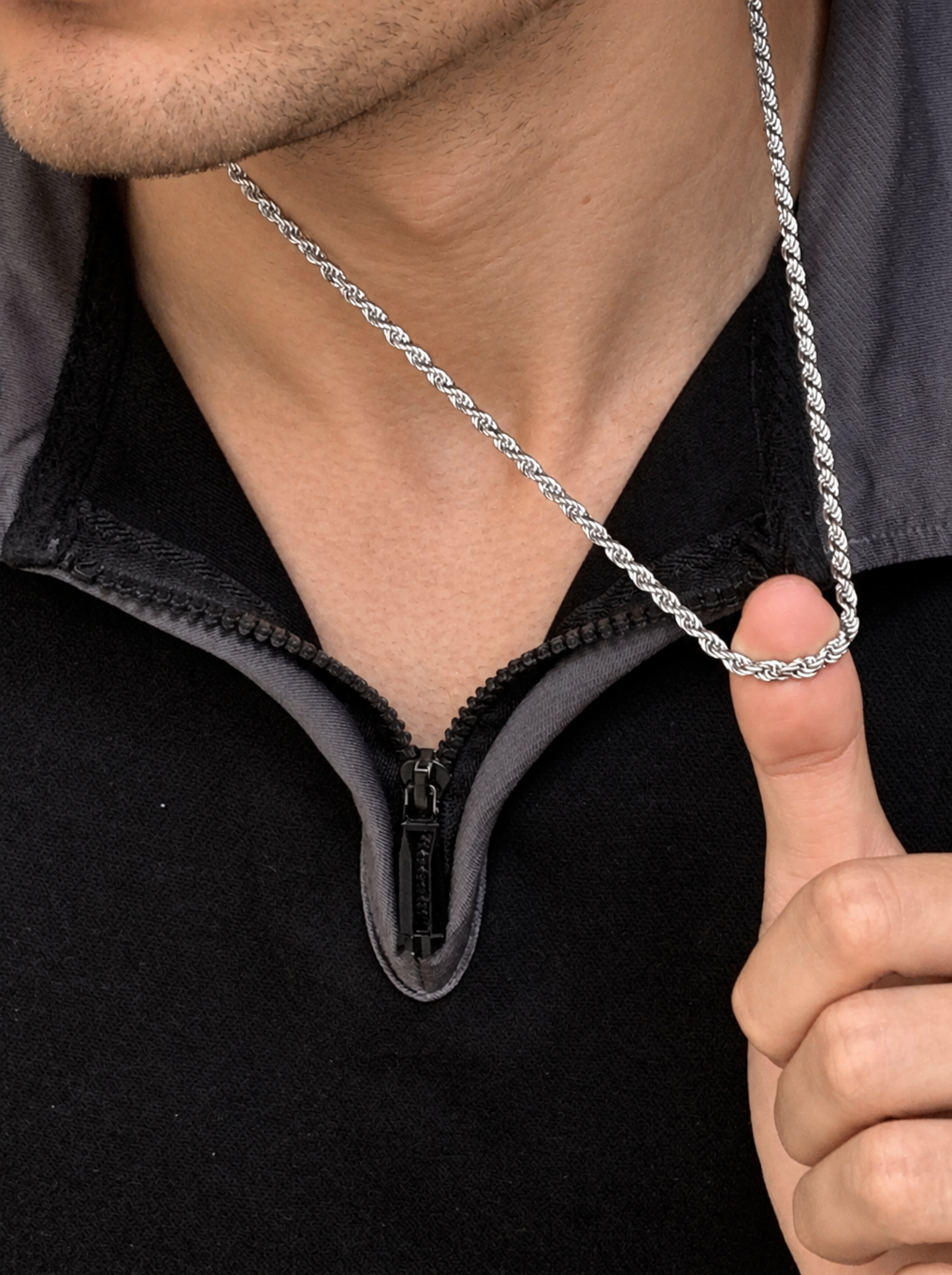 Model lifting a silver-tone rope chain with one finger above a black zip collar