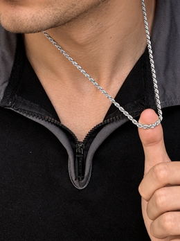 Model lifting a silver-tone rope chain with one finger above a black zip collar