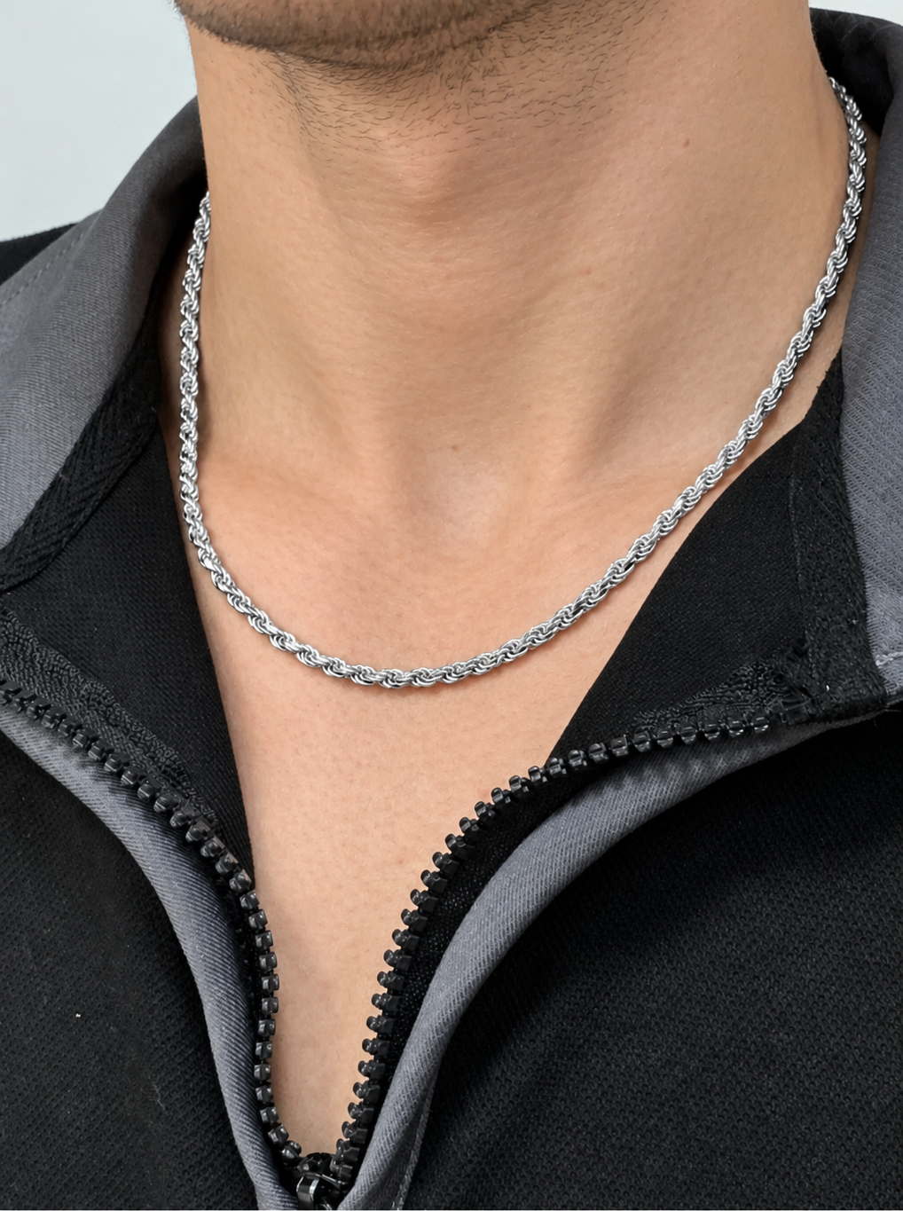 Silver-tone rope chain worn at the neck above a black zip collar