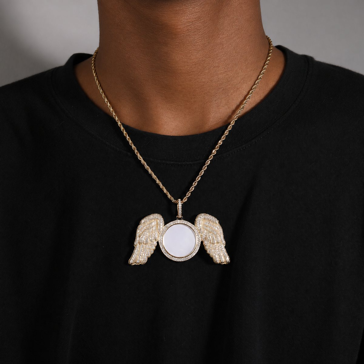 Gold-tone angel wings photo pendant worn over a black shirt