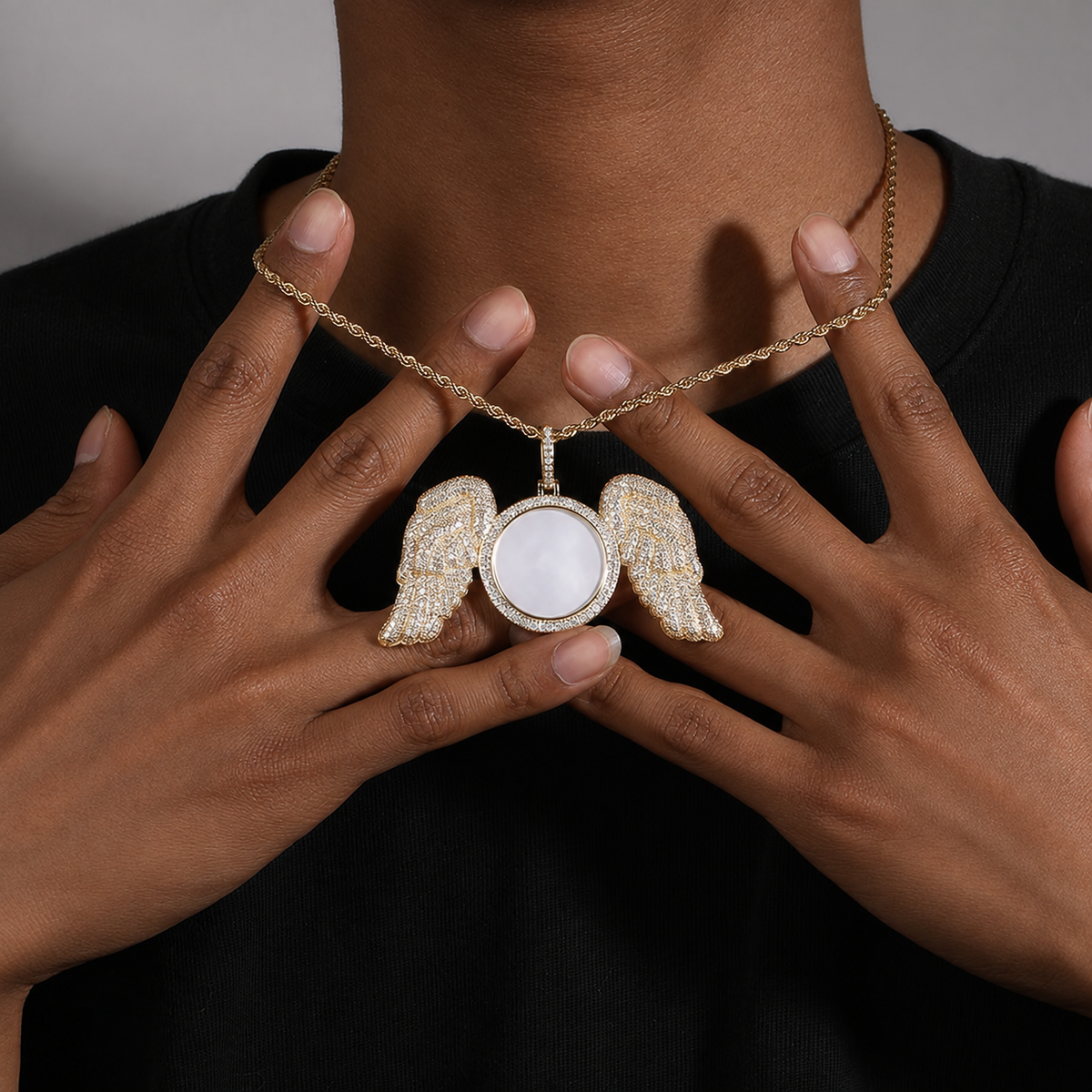 Hands holding a gold-tone angel wings photo pendant in front of a black shirt