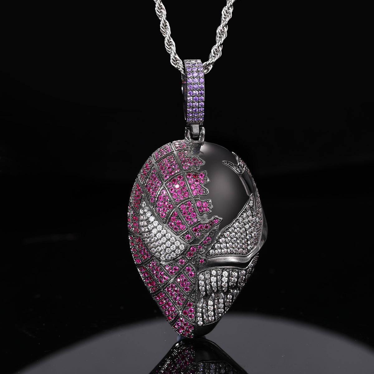 Dark silver-tone mask pendant with pink and clear stones, suspended over a black reflective surface