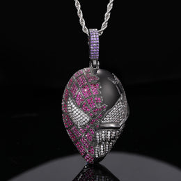 Dark silver-tone mask pendant with pink and clear stones, suspended over a black reflective surface