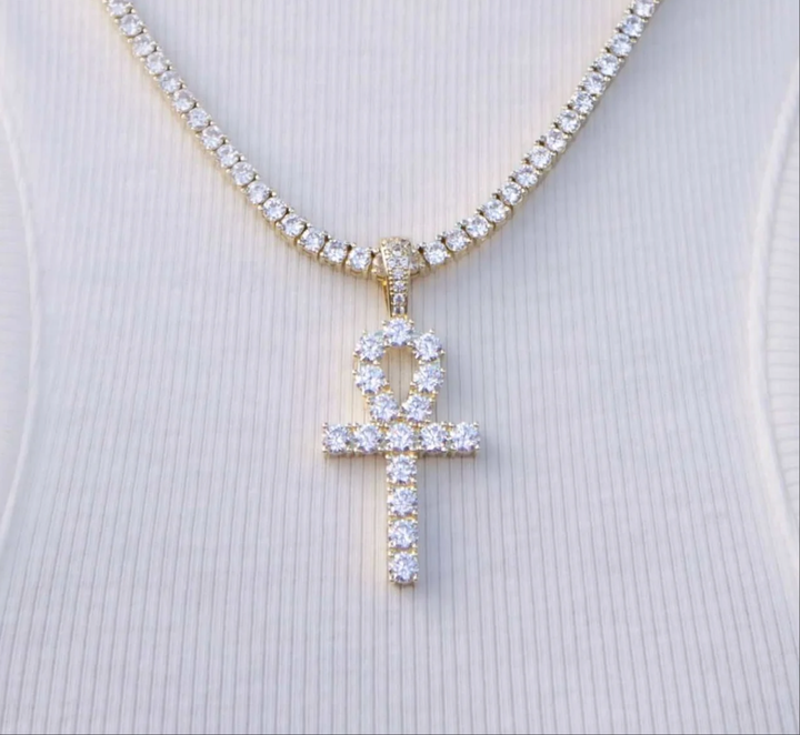 Gold-tone stone-set ankh pendant on a chain against a white shirt