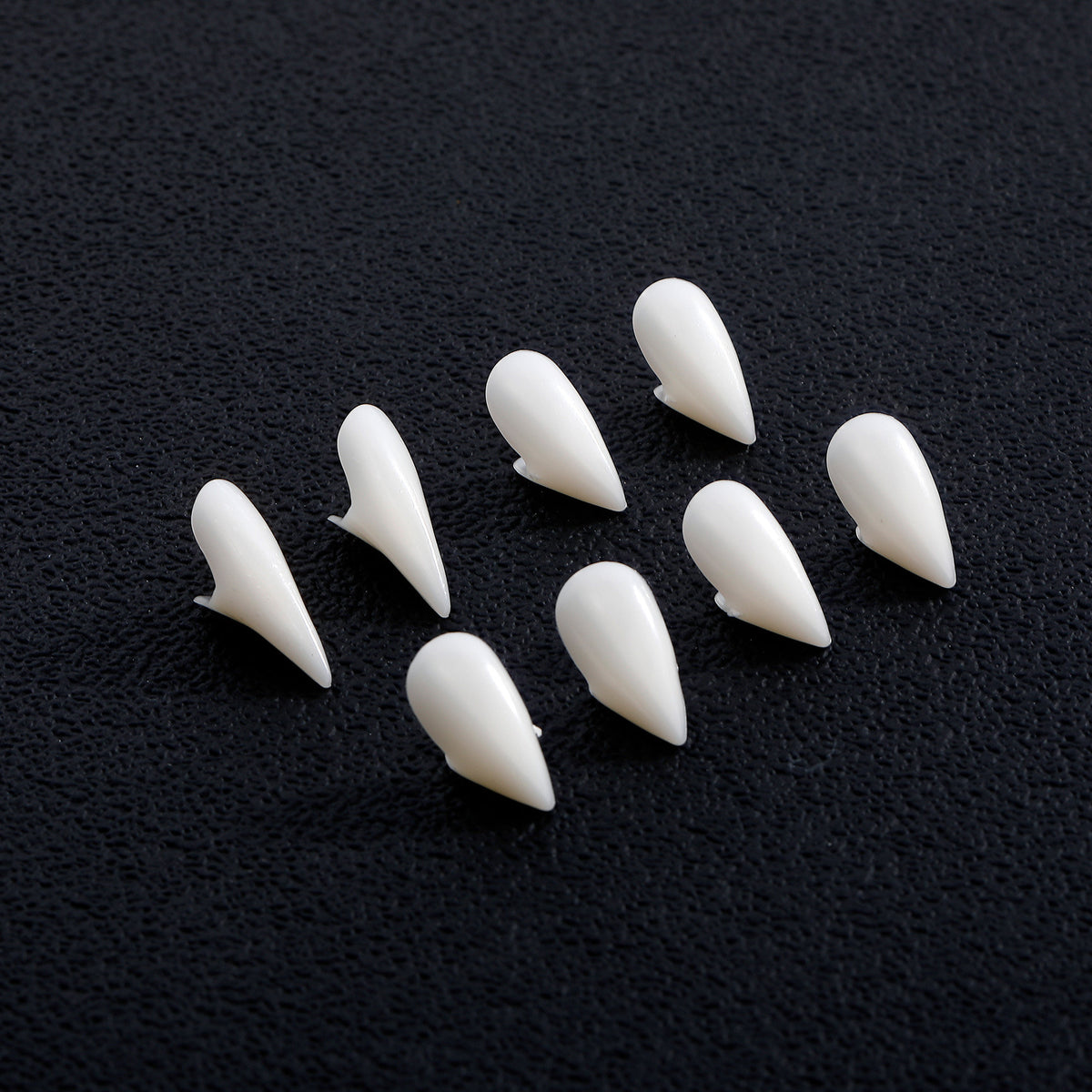Four pairs of white vampire fangs compared on a dark background